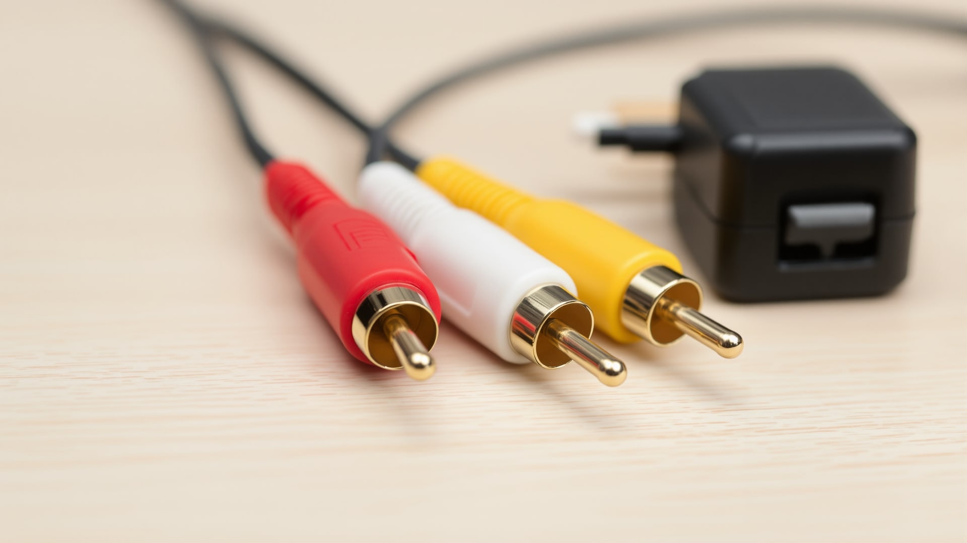 Red, white and yellow RCA phono connectors on a camera AV cable beside a 12v power supply